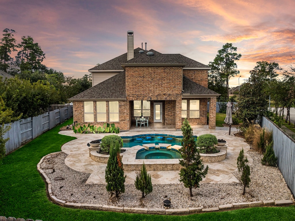 back house at dusk featuring an in ground hot tub, a yard, and a patio area