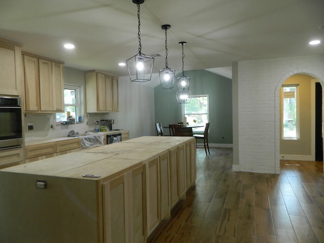 kitchen with arched walkways, dark wood finished floors, stainless steel appliances, light brown cabinetry, and a kitchen island