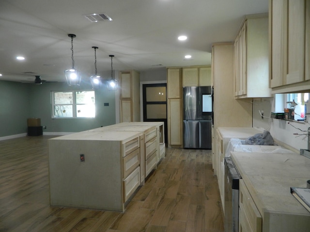 kitchen with freestanding refrigerator, wood finished floors, a center island, and light brown cabinetry