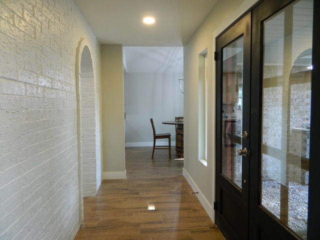 hall featuring brick wall, baseboards, wood finished floors, and french doors