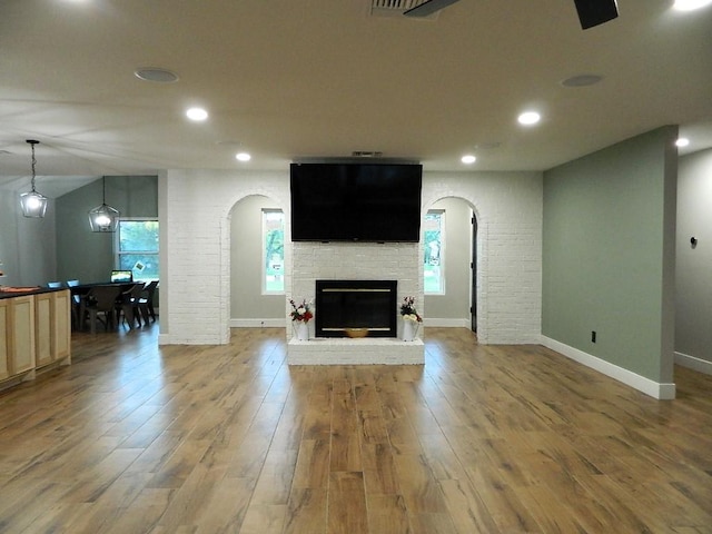 unfurnished living room with arched walkways, a glass covered fireplace, wood finished floors, and recessed lighting