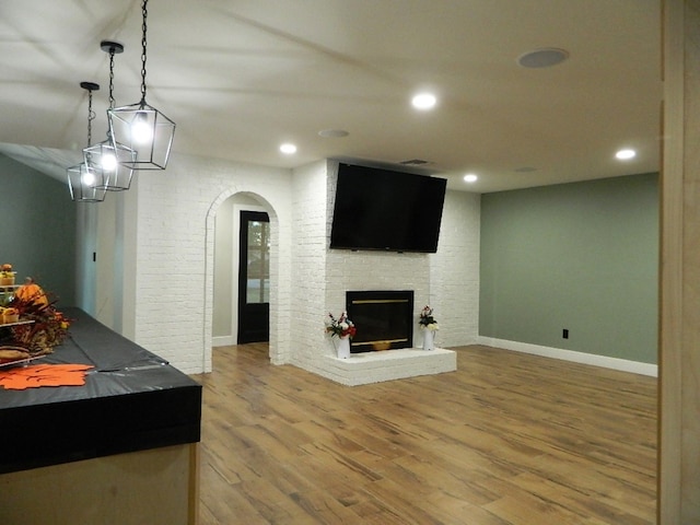 interior space with arched walkways, baseboards, brick wall, wood finished floors, and a brick fireplace