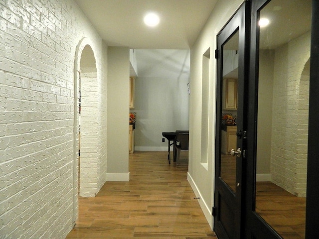 hallway with brick wall, wood finished floors, and baseboards