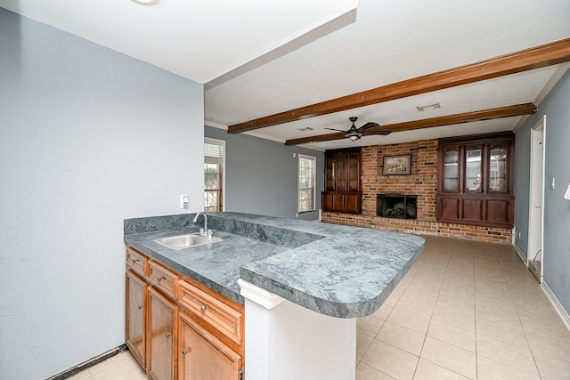 kitchen featuring beam ceiling, sink, kitchen peninsula, and a brick fireplace