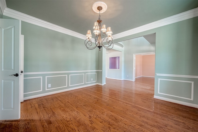 unfurnished room with hardwood / wood-style floors, an inviting chandelier, and crown molding