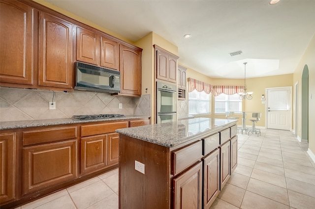 kitchen featuring decorative backsplash, a kitchen island, appliances with stainless steel finishes, light tile patterned flooring, and light stone counters