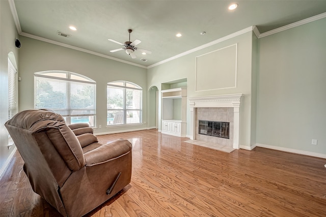 living room with built in shelves, ceiling fan, crown molding, a fireplace, and hardwood / wood-style flooring