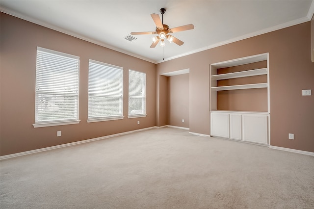 carpeted spare room with built in shelves, ceiling fan, crown molding, and a healthy amount of sunlight