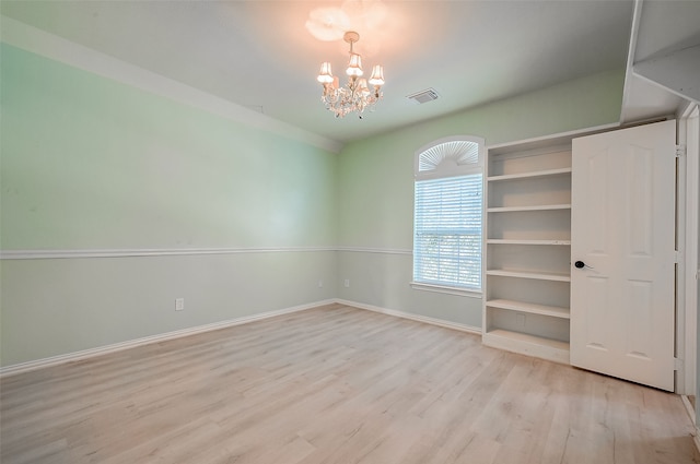 spare room featuring light wood-type flooring and a notable chandelier