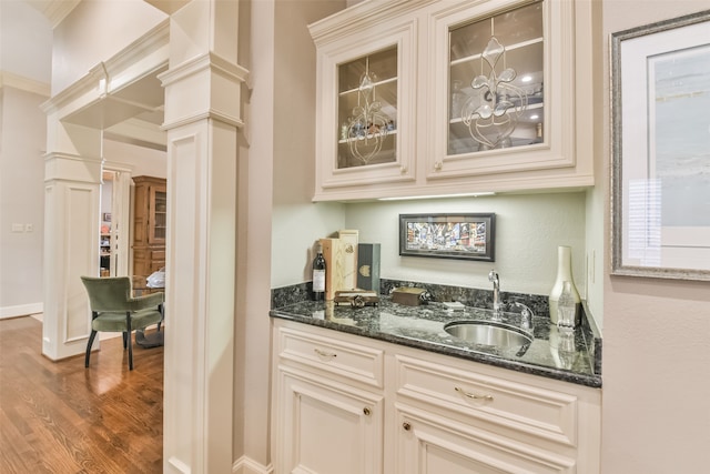 kitchen featuring cream cabinetry, dark wood-type flooring, dark stone counters, decorative columns, and sink