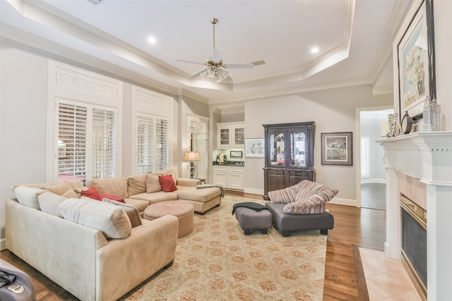 living room featuring a fireplace, crown molding, a tray ceiling, ceiling fan, and hardwood / wood-style flooring