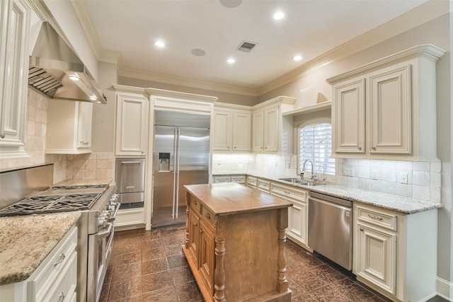 kitchen featuring wall chimney exhaust hood, light stone countertops, premium appliances, a center island, and sink