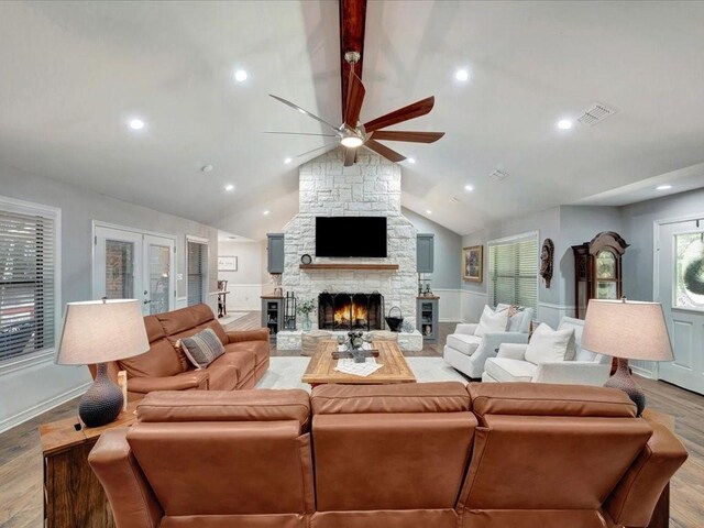 living room featuring lofted ceiling, light hardwood / wood-style floors, and a stone fireplace