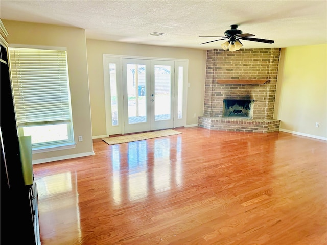 unfurnished living room featuring a brick fireplace, a wealth of natural light, light hardwood / wood-style floors, and ceiling fan