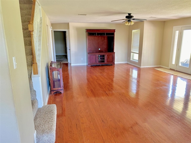 unfurnished living room with ceiling fan, hardwood / wood-style flooring, a textured ceiling, and a wealth of natural light