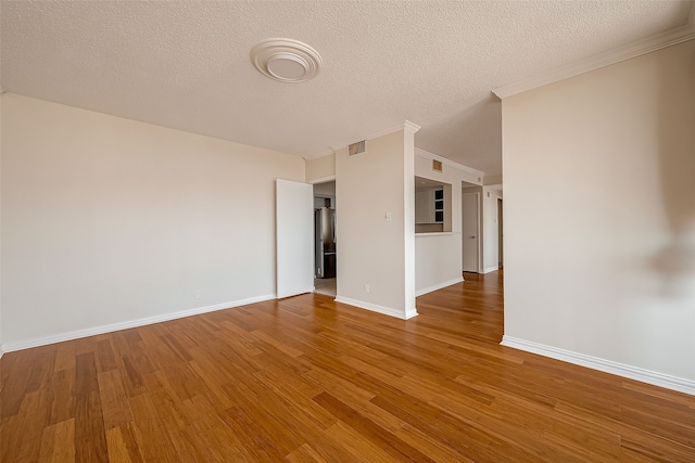 empty room with wood-type flooring, a textured ceiling, and crown molding