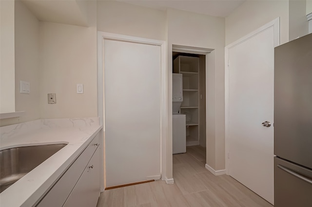 interior space with white cabinets, stainless steel refrigerator, and stacked washer / dryer