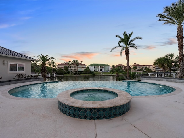 pool at dusk featuring pool water feature, a patio, and an in ground hot tub