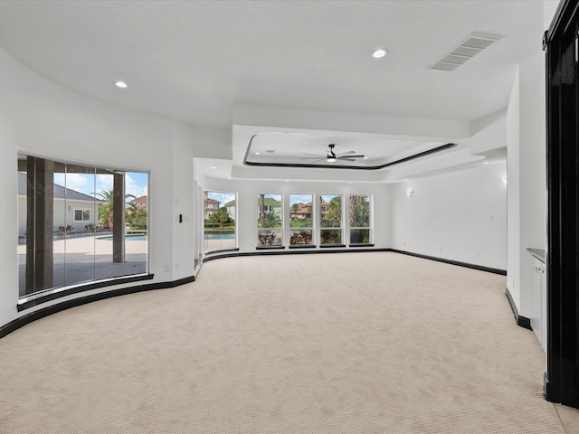 carpeted empty room featuring a tray ceiling, ceiling fan, and a healthy amount of sunlight