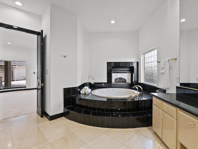 bathroom with tiled tub, vanity, a tiled fireplace, and tile patterned flooring