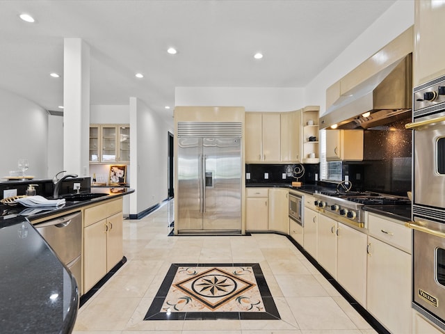 kitchen with light tile patterned floors, built in appliances, wall chimney range hood, and sink