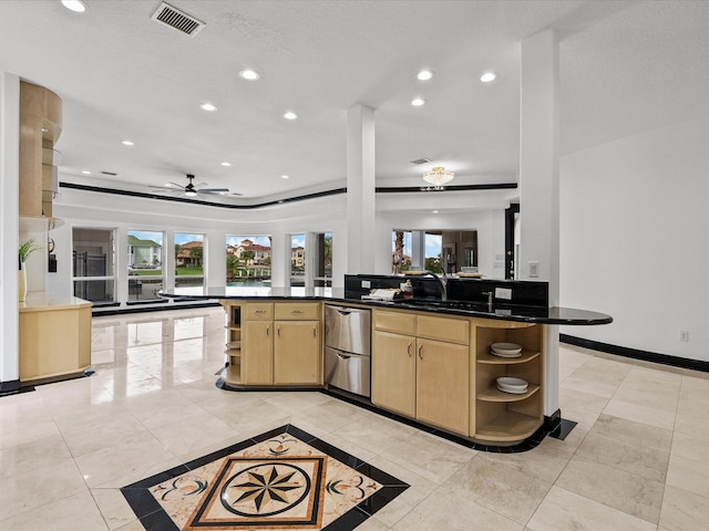 kitchen featuring ceiling fan, sink, kitchen peninsula, light brown cabinetry, and dark stone counters