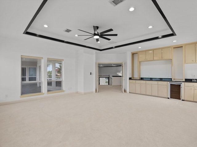 unfurnished living room featuring ceiling fan, beverage cooler, a tray ceiling, and light carpet