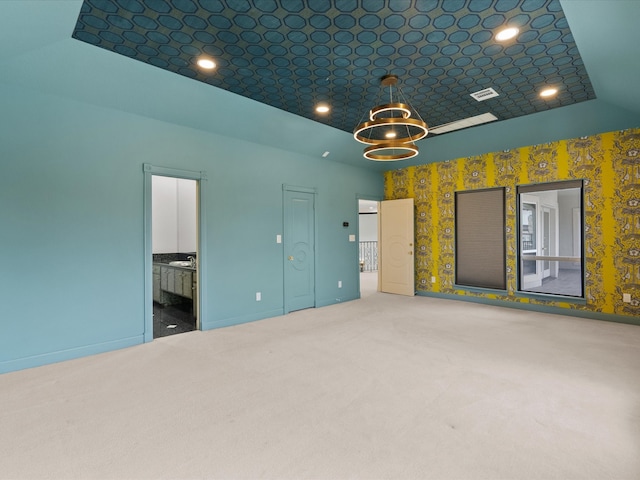 interior space with a tray ceiling, connected bathroom, a chandelier, and carpet