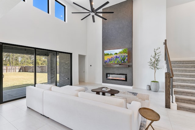 tiled living room featuring ceiling fan, a towering ceiling, a fireplace, and a wealth of natural light