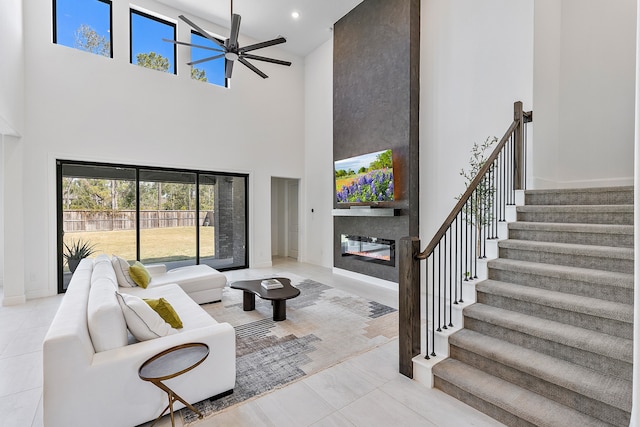 tiled living room featuring ceiling fan, a large fireplace, and a towering ceiling