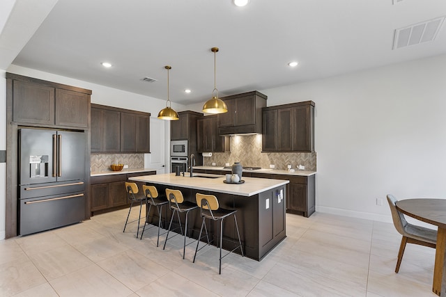 kitchen with dark brown cabinets, an island with sink, appliances with stainless steel finishes, and a breakfast bar area