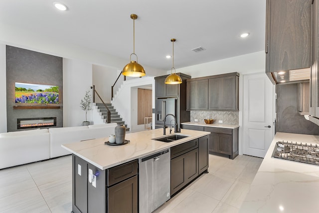 kitchen with sink, light stone countertops, a fireplace, decorative light fixtures, and stainless steel appliances