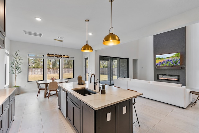 kitchen with pendant lighting, light tile patterned flooring, a kitchen island with sink, sink, and a large fireplace