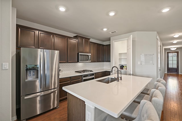 kitchen featuring an island with sink, sink, dark brown cabinets, stainless steel appliances, and dark hardwood / wood-style floors