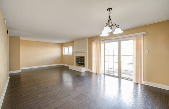 unfurnished living room featuring a notable chandelier, a tiled fireplace, and dark hardwood / wood-style flooring