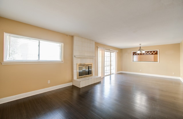 unfurnished living room with a notable chandelier, a fireplace, and dark wood-type flooring