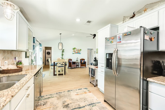 kitchen with appliances with stainless steel finishes, light hardwood / wood-style floors, white cabinetry, and stacked washer / drying machine