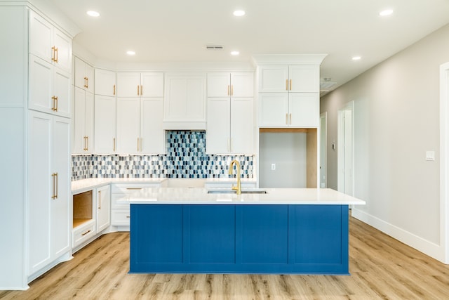 kitchen with light hardwood / wood-style flooring, white cabinets, and a kitchen island with sink