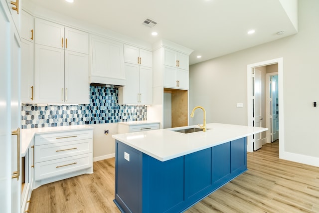 kitchen featuring a center island with sink, sink, backsplash, white cabinetry, and light hardwood / wood-style flooring