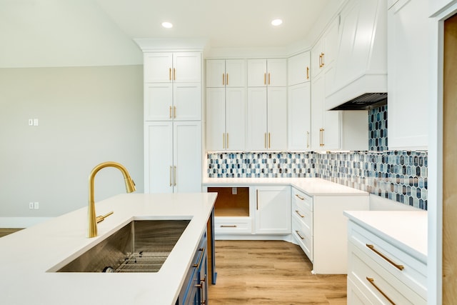 kitchen featuring premium range hood, white cabinetry, backsplash, sink, and light hardwood / wood-style flooring