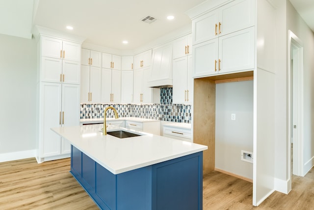 kitchen featuring light hardwood / wood-style floors, decorative backsplash, sink, a kitchen island with sink, and white cabinetry