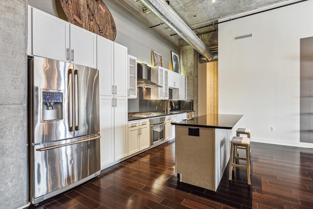 kitchen featuring appliances with stainless steel finishes, white cabinetry, a kitchen breakfast bar, dark hardwood / wood-style flooring, and wall chimney exhaust hood