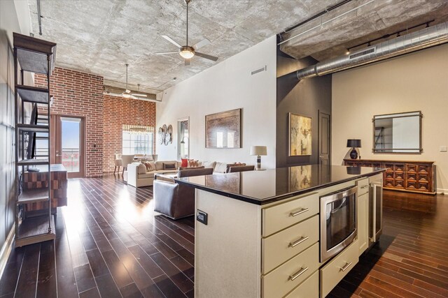 kitchen with brick wall, a kitchen island, stainless steel microwave, dark hardwood / wood-style flooring, and a high ceiling