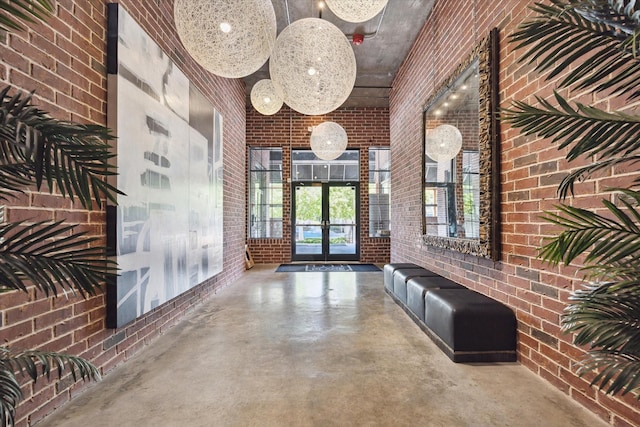 hallway featuring concrete flooring, french doors, a high ceiling, and brick wall