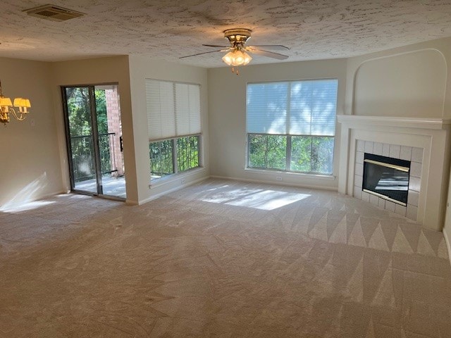 unfurnished living room with a textured ceiling, ceiling fan with notable chandelier, a fireplace, and light colored carpet