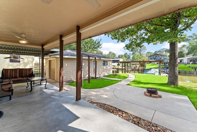 view of patio / terrace featuring ceiling fan, a storage shed, a water view, and an outdoor fire pit