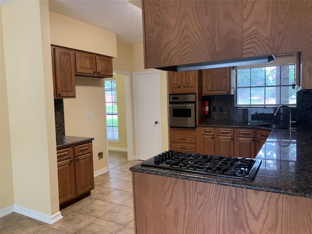 kitchen with dark stone counters, plenty of natural light, sink, black gas stovetop, and stainless steel oven