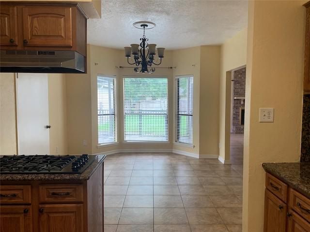 kitchen with dark stone countertops, light tile patterned floors, range hood, gas cooktop, and a chandelier