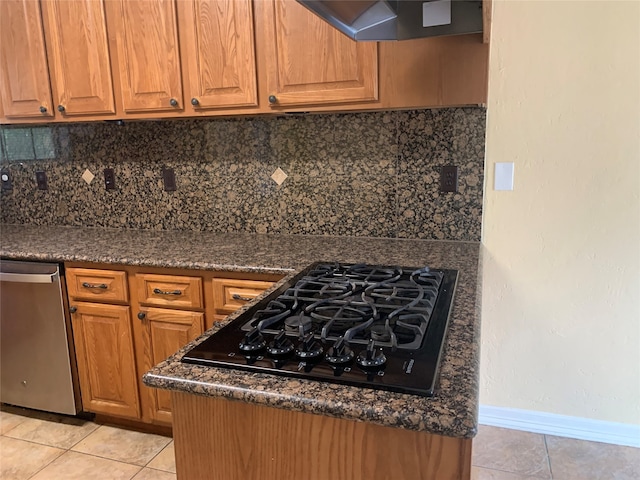 kitchen with black gas stovetop, wall chimney exhaust hood, decorative backsplash, light tile patterned floors, and dark stone countertops