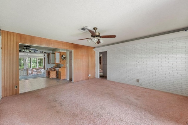 unfurnished living room featuring brick wall, wooden walls, carpet, and ceiling fan